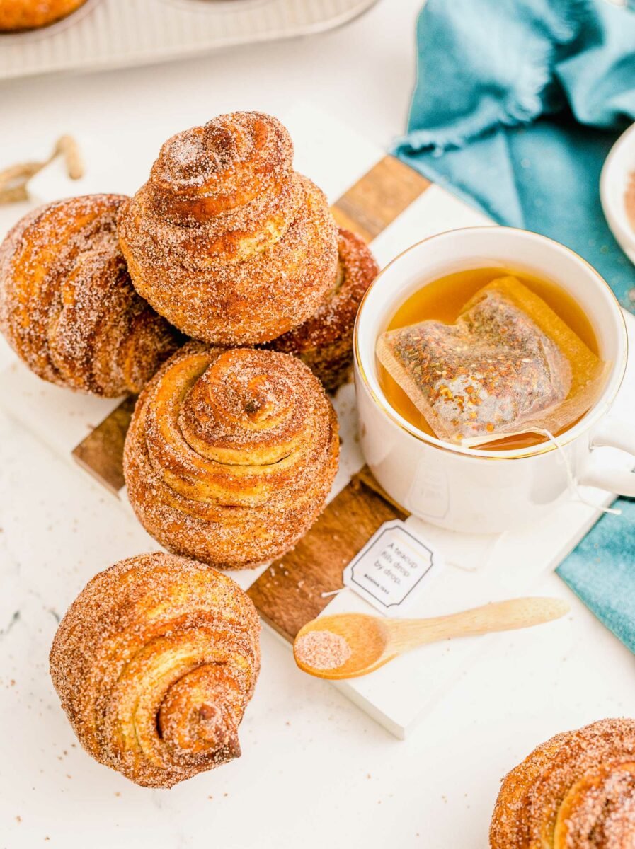 Several cinnamon sugar cruffins are placed on a white countertop next to a cup of tea.