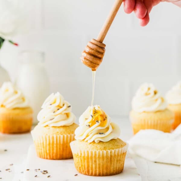 Honey is being drizzled onto a frosted cupcake.