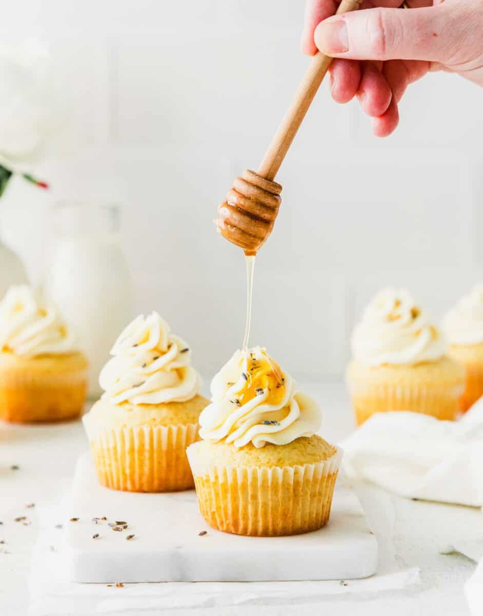 Honey is being drizzled onto a frosted cupcake. 