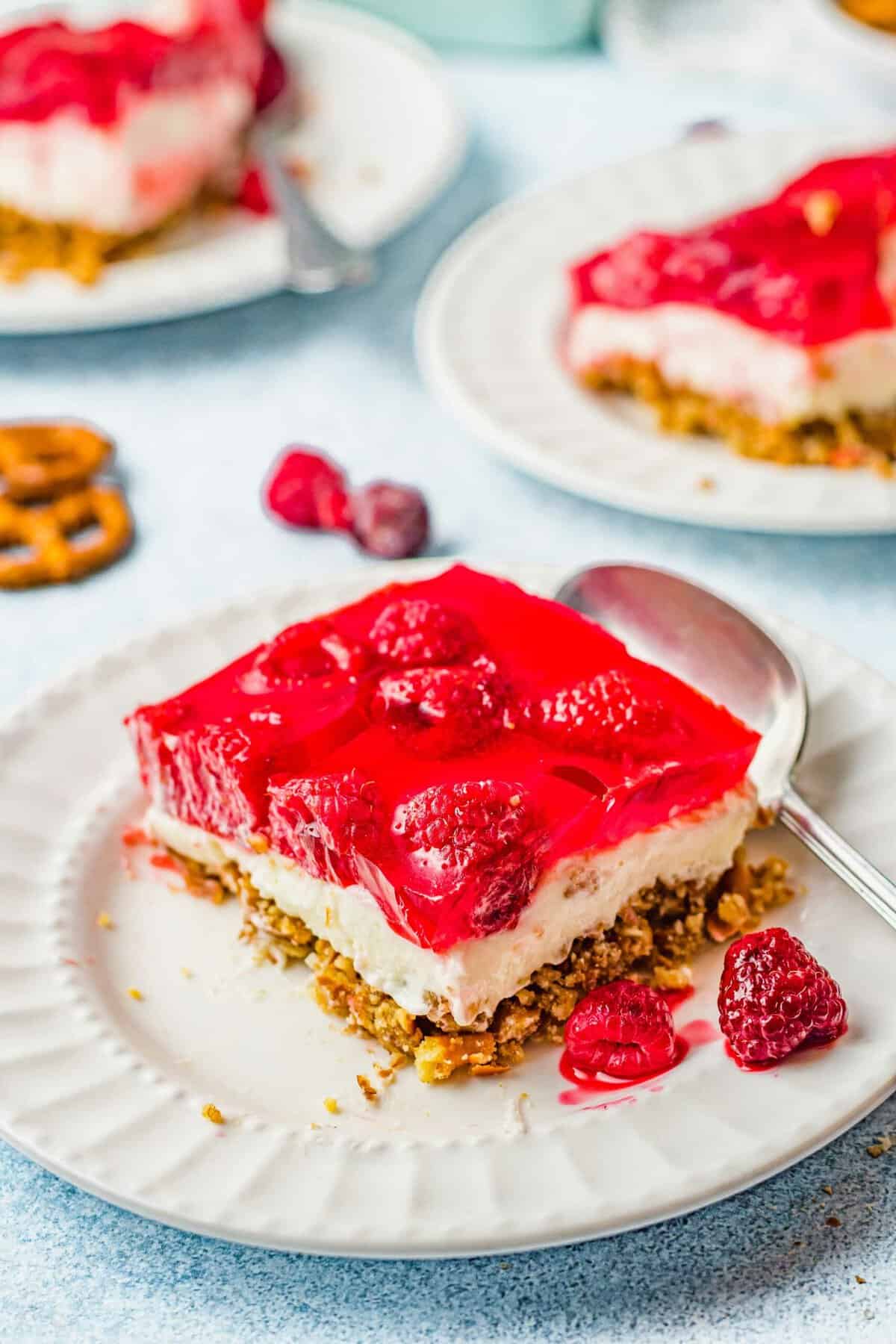 Square of raspberry pretzel salad on plate with spoon