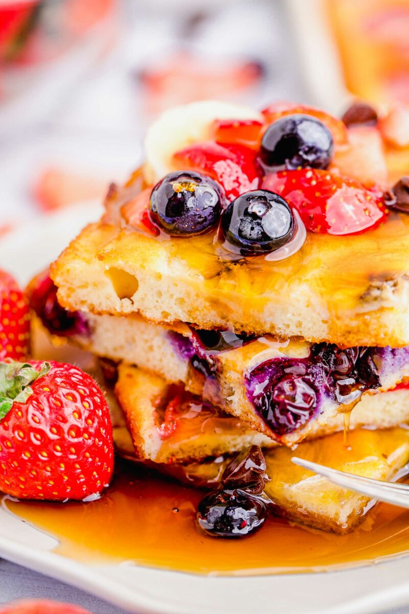 Fresh strawberries are placed next to a stack of square cut pancakes topped with maple syrup.