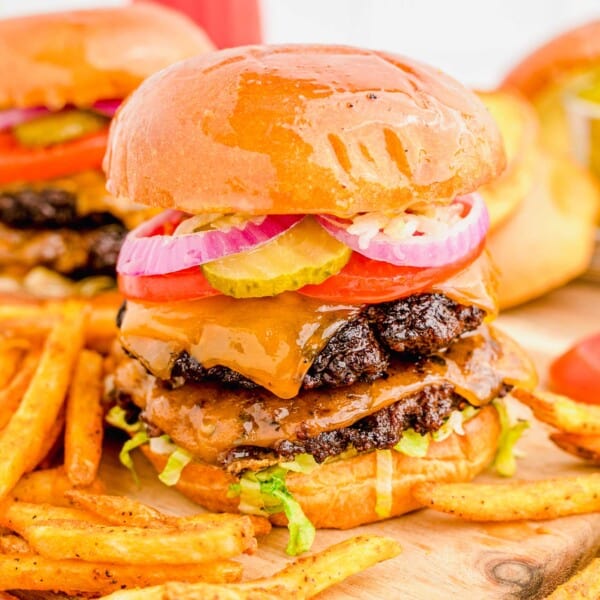 A smash burger is placed on a wooden cutting board next to some fries.