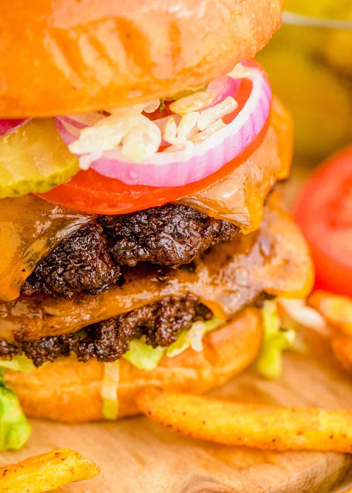 Two smashed burger patties with cheese are between two buns, with onions, tomatoes, and lettuce.