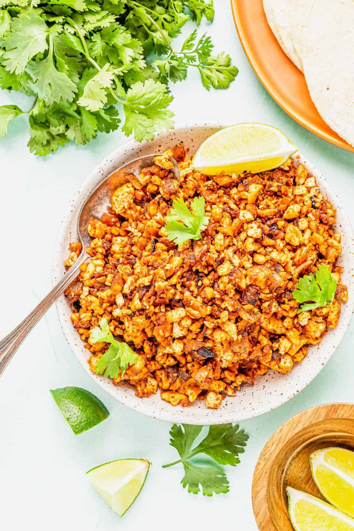 Bowl of tofu chorizo with spoon, garnished with lime wedge and cilantro