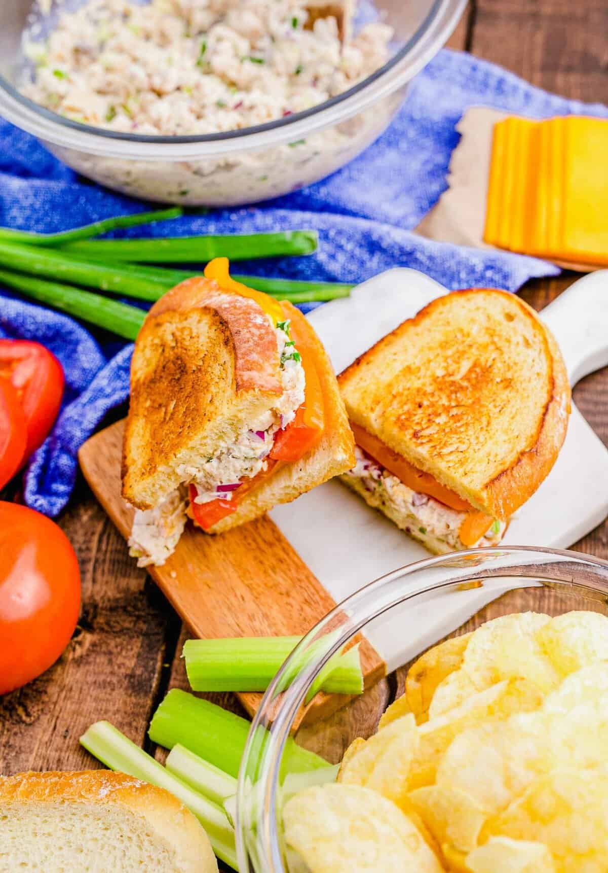 Halved tuna melt sandwich on small cutting board, surrounded by sandwich ingredients