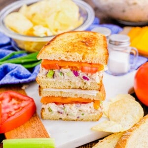 Two stacked tuna melt halves, surrounded by potato chips and sandwich ingredients