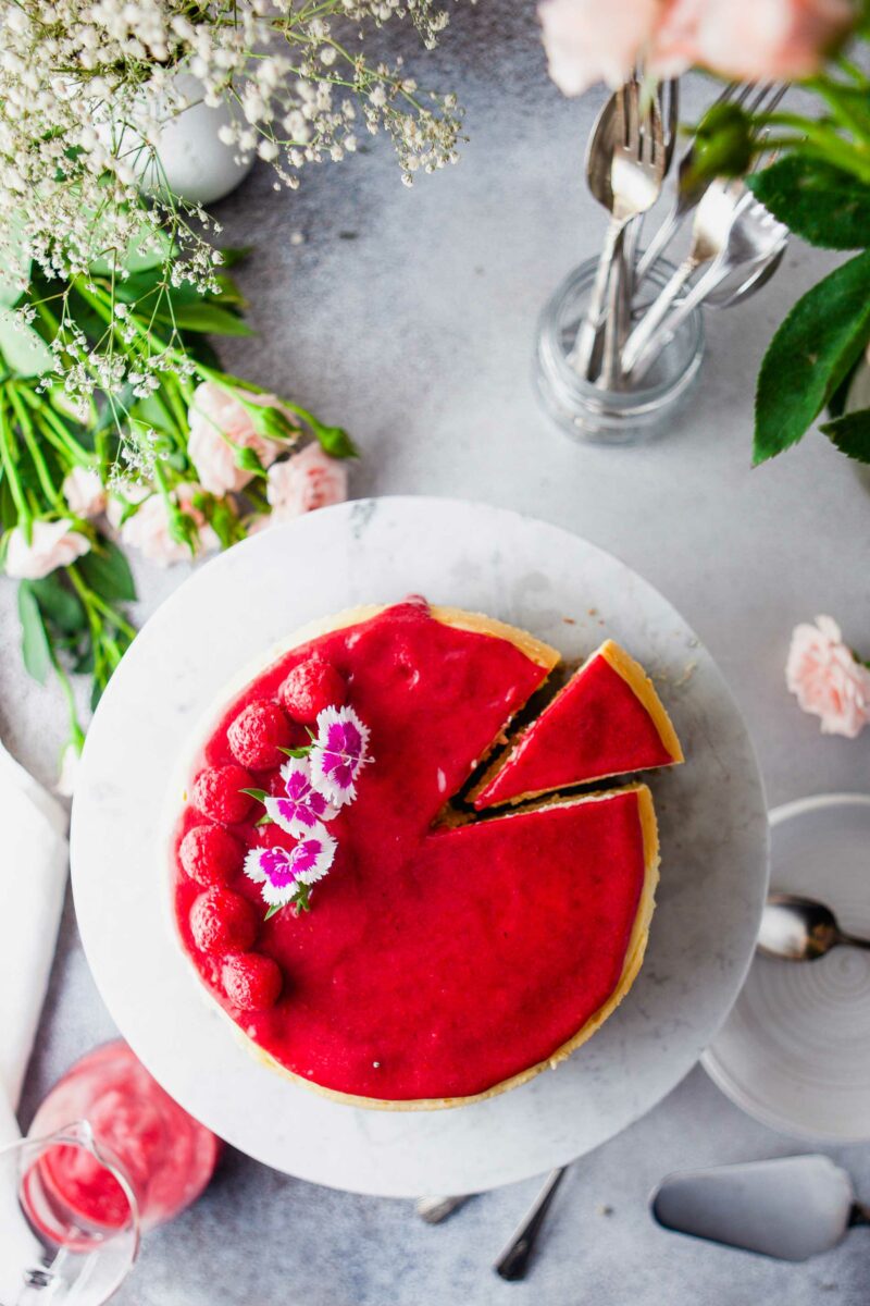 A raspberry cheesecake is garnished with extra berries and edible flowers. 