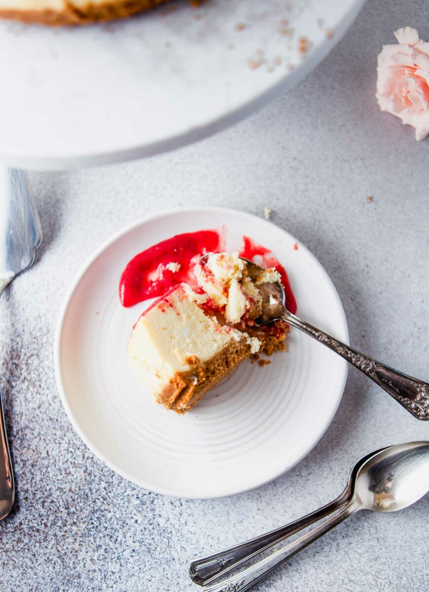 A slice of cheesecake is being broken up by a spoon. 
