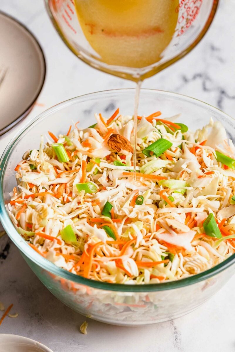 Asian ramen salad sauce being poured on salad in a clear bowl.