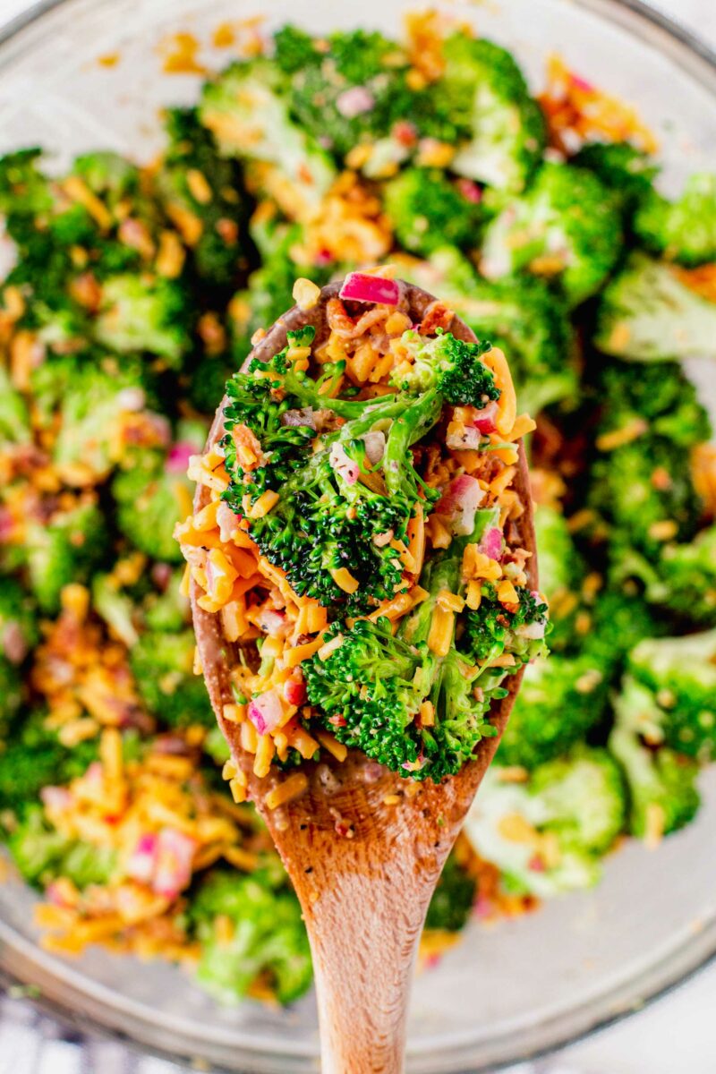 A wooden spoon has lifted a portion of broccoli salad from the bowl.