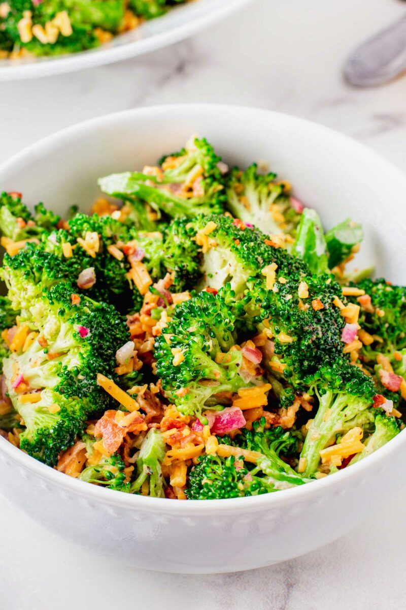 A white bowl is filled with freshly made broccoli salad. 