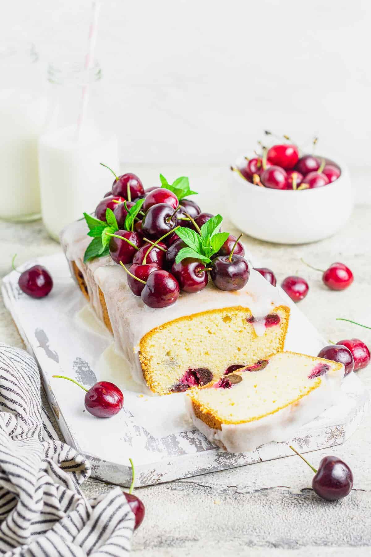 Cherry amaretto loaf cake on rustic board, topped with cherries and mint