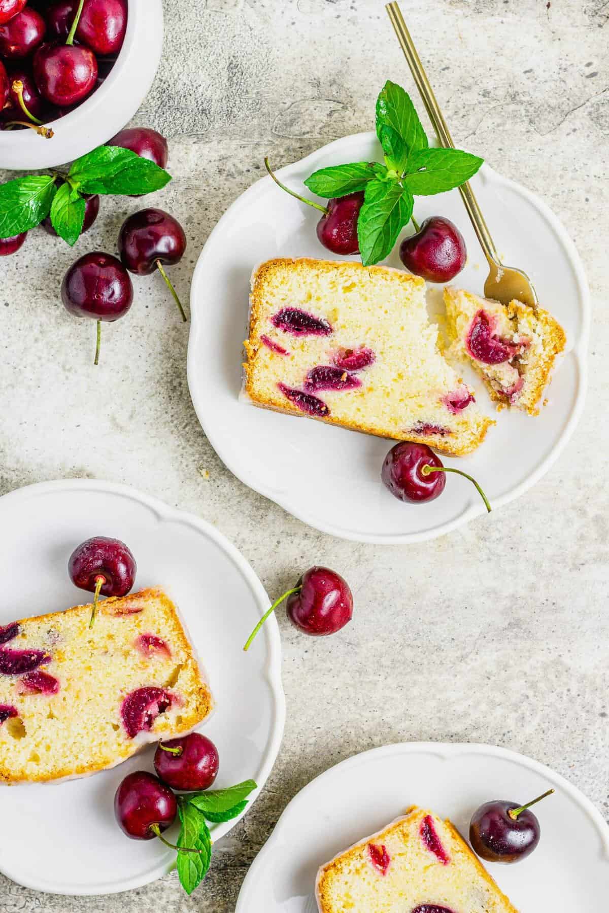 Three plates with slices of cherry amaretto loaf cake and fresh cherries