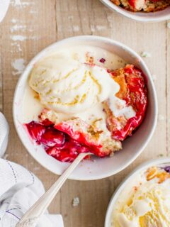 Overhead view of cherry cobbler in bowl with ice cream
