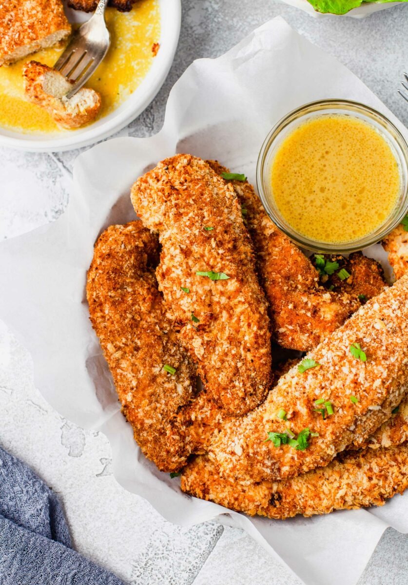 A fork has pierced a bite sized piece of chicken and is resting on a plate next to other tenders. 