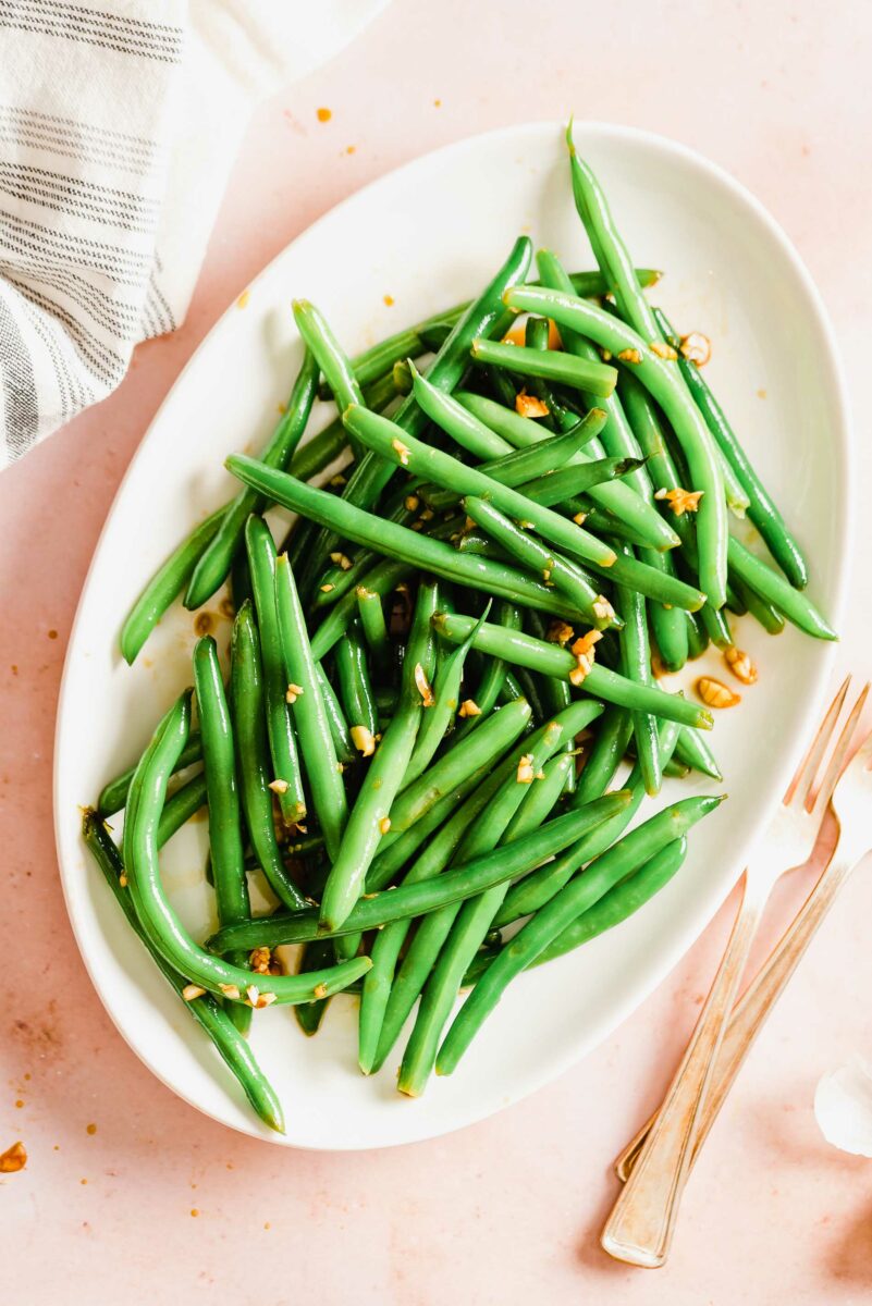 An oval shaped white plate is topped with a pile of marinated green beans.