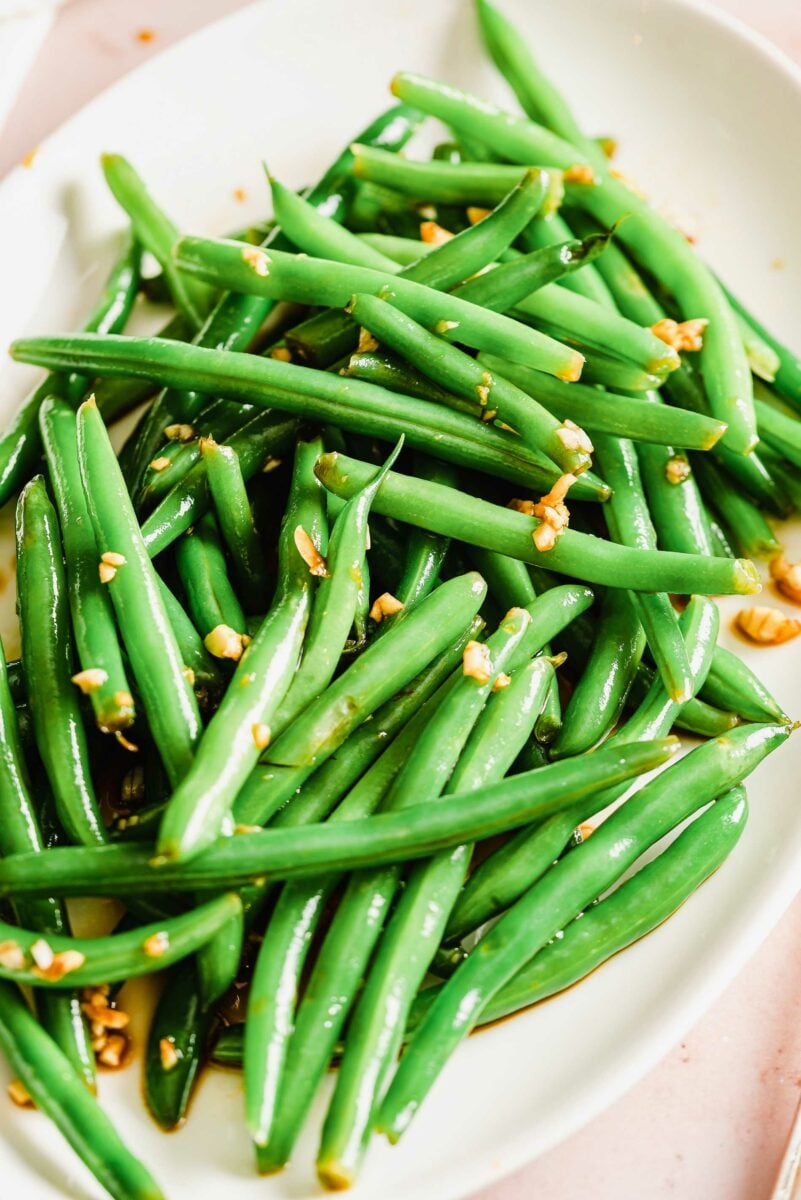 A close up of a white plate that is has a large serving of garlic and soy green beans. 