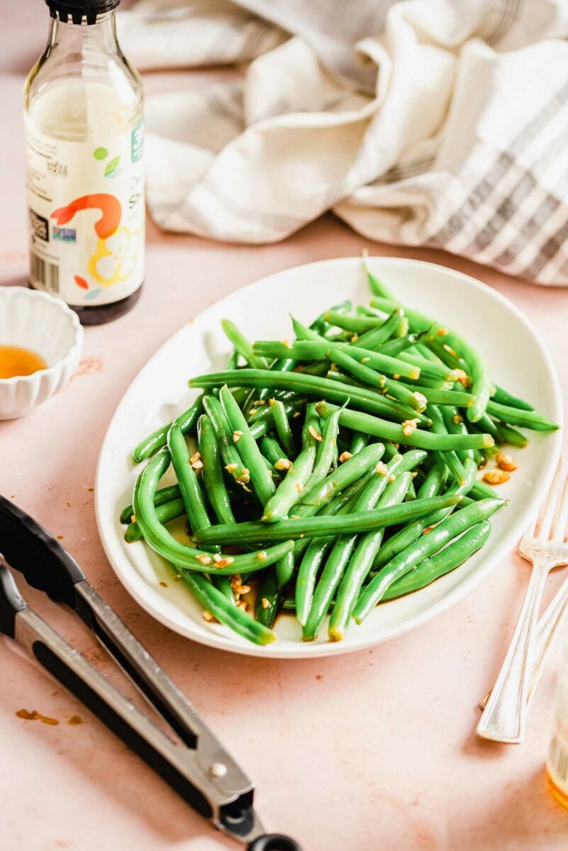 Tongs, soy sauce, and utensils are placed next to a serving of green beans.