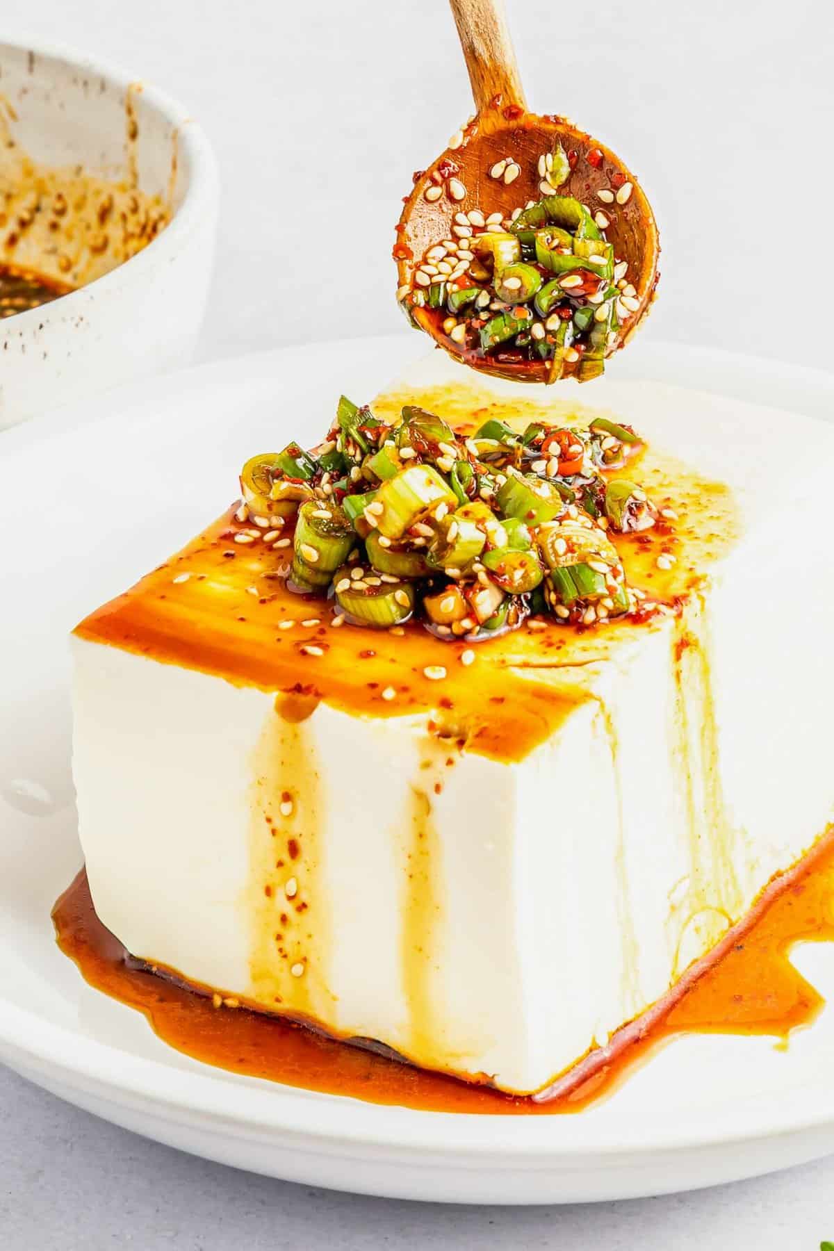 Sauce is being drizzled over a block of silken tofu.