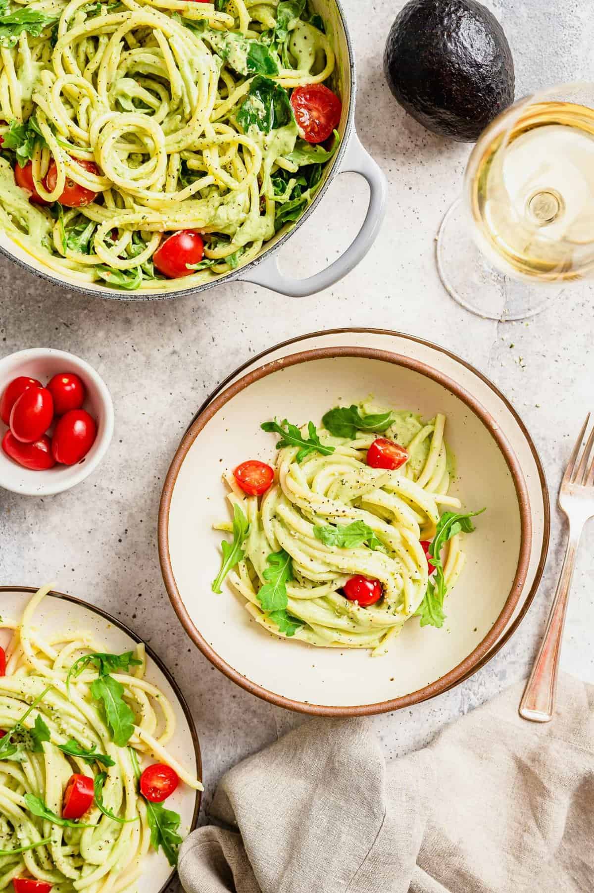 Creamy avocado pasta in bowls and pan with glass of wine
