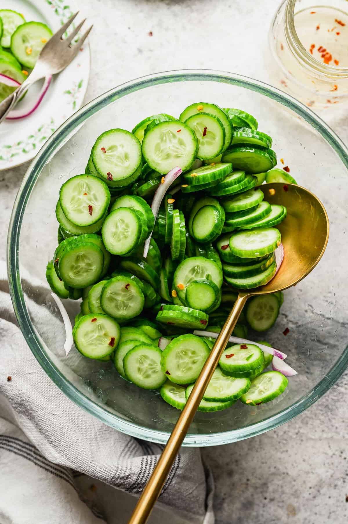 Overhead view of cucumber salad in large glass bowl with gold serving spoon