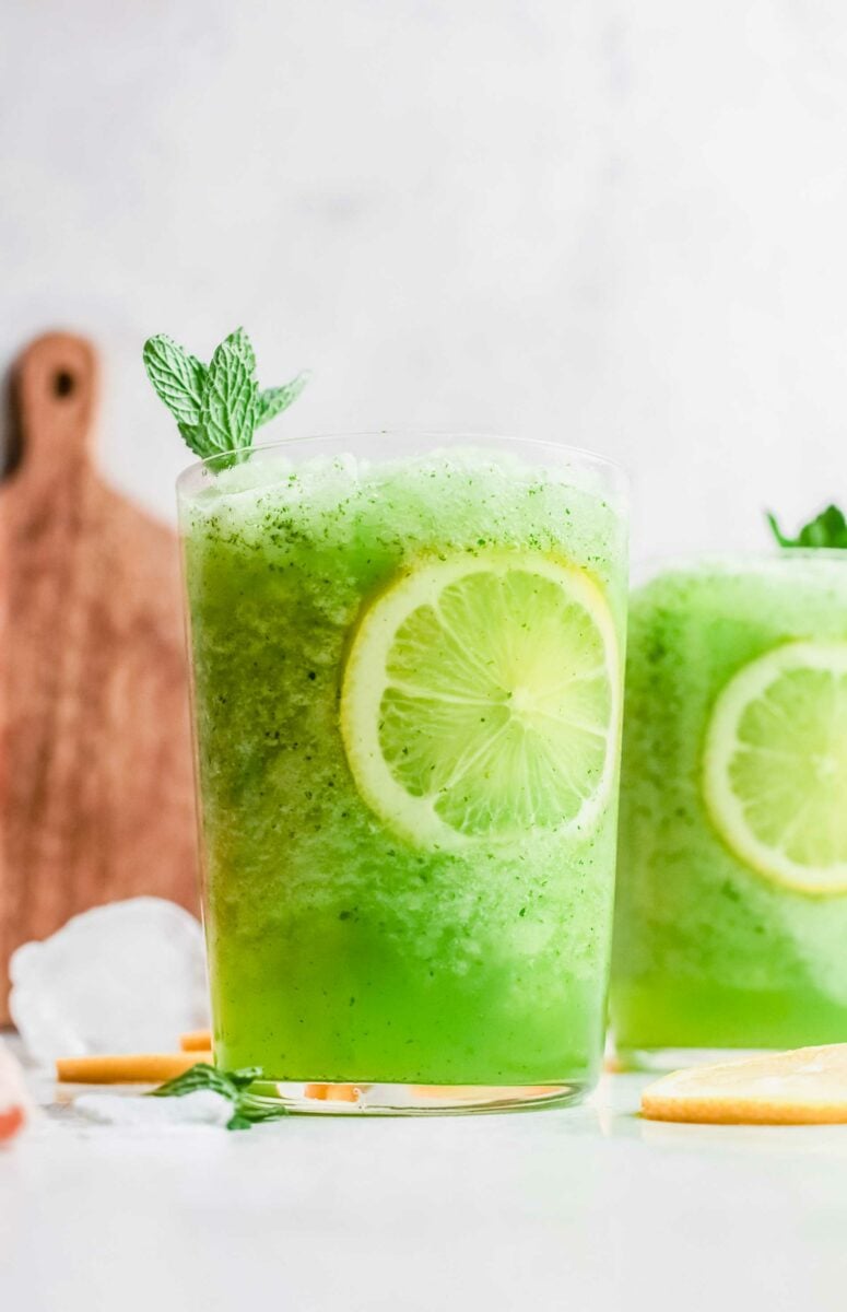 A vibrant green frozen lemonade is served in a clear glass with a lemon slice.
