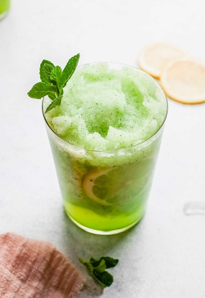 A glass of frozen mint lemonade is placed on a white countertop. 