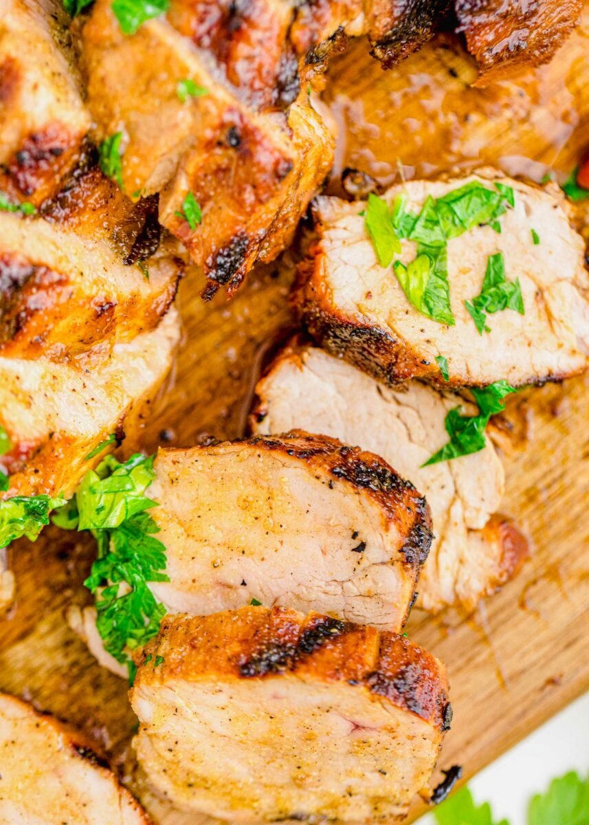 Slices of pork tenderloin are presented on a wooden cutting board. 