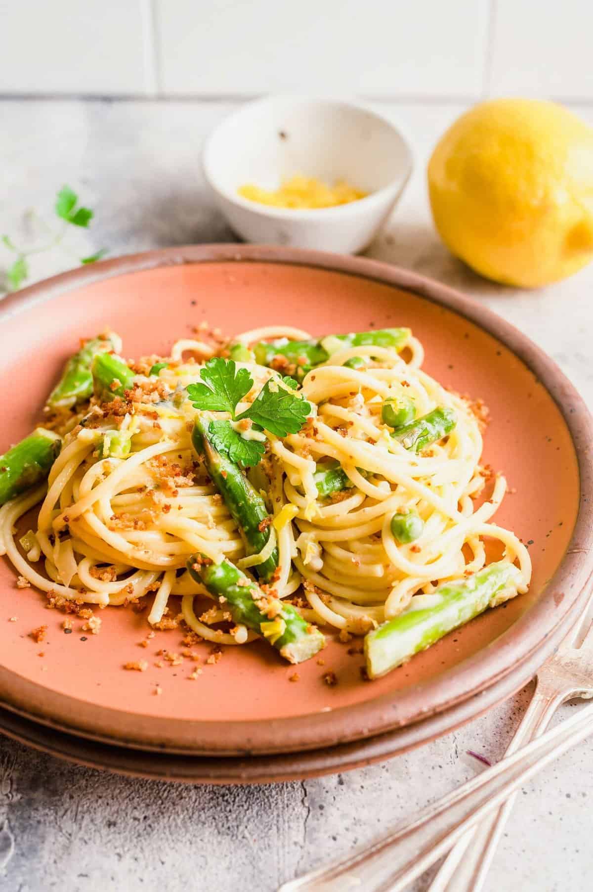 Asparagus and lemon pasta on plate with lemon and bowl of zest in background