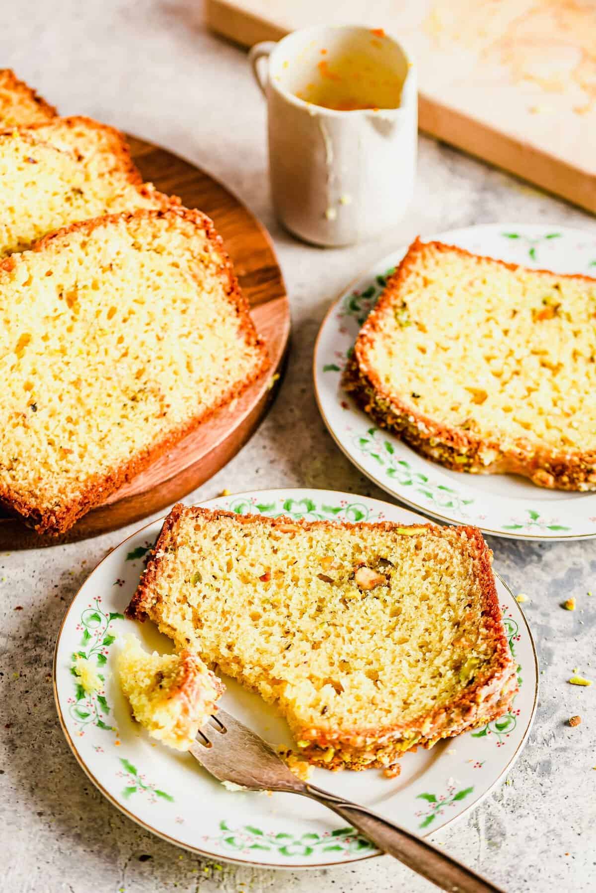 Slices of orange pistachio bread on two plates and wood cutting board