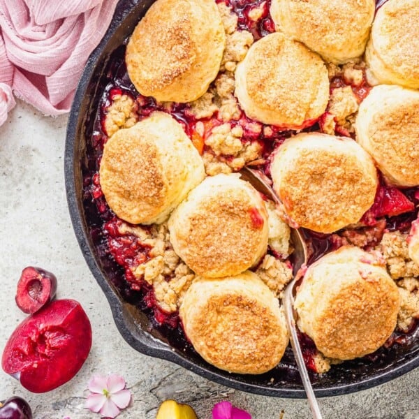 Overhead view of spoon digging into cast iron skillet of fruit cobbler