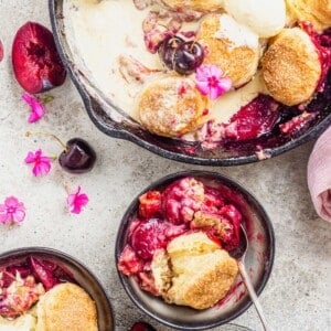 Biscuit-topped stone fruit cobbler in cast iron pan and two serving bowls