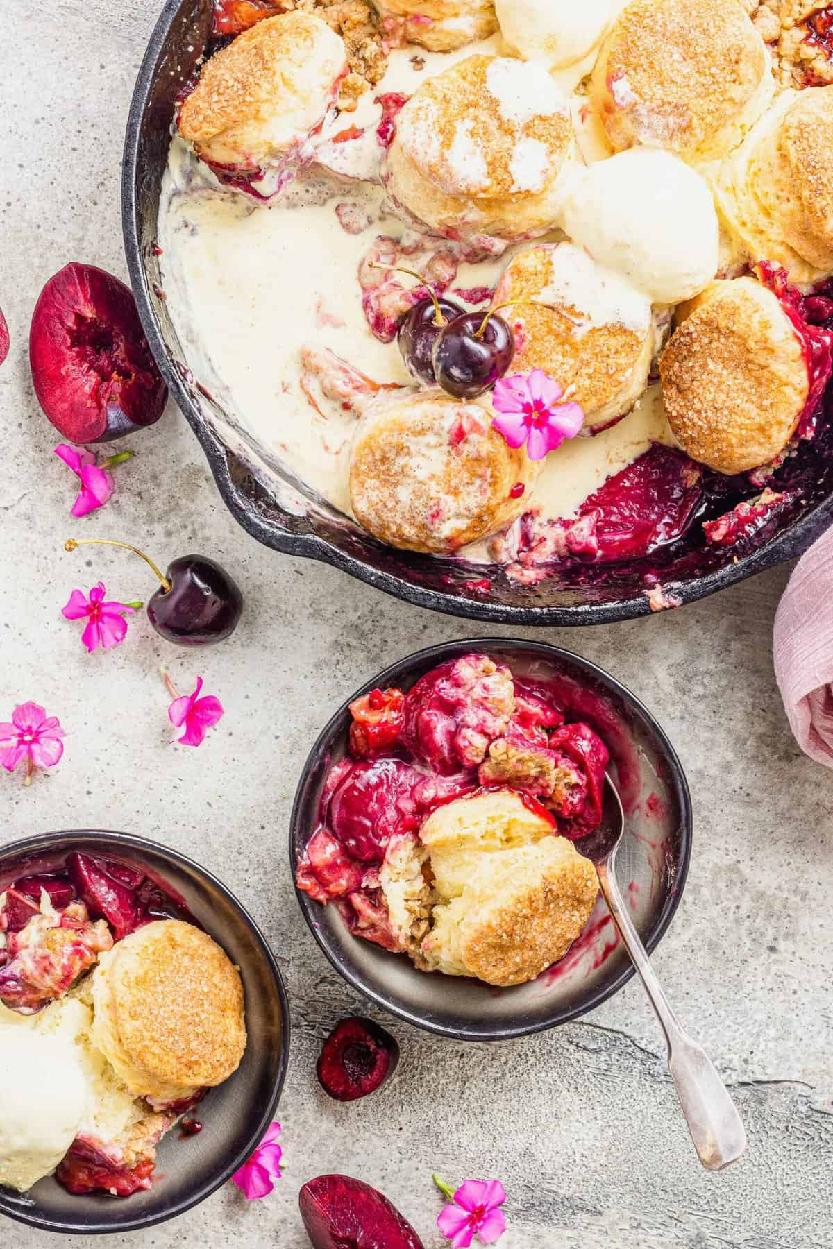 Biscuit-topped stone fruit cobbler in cast iron pan and two serving bowls