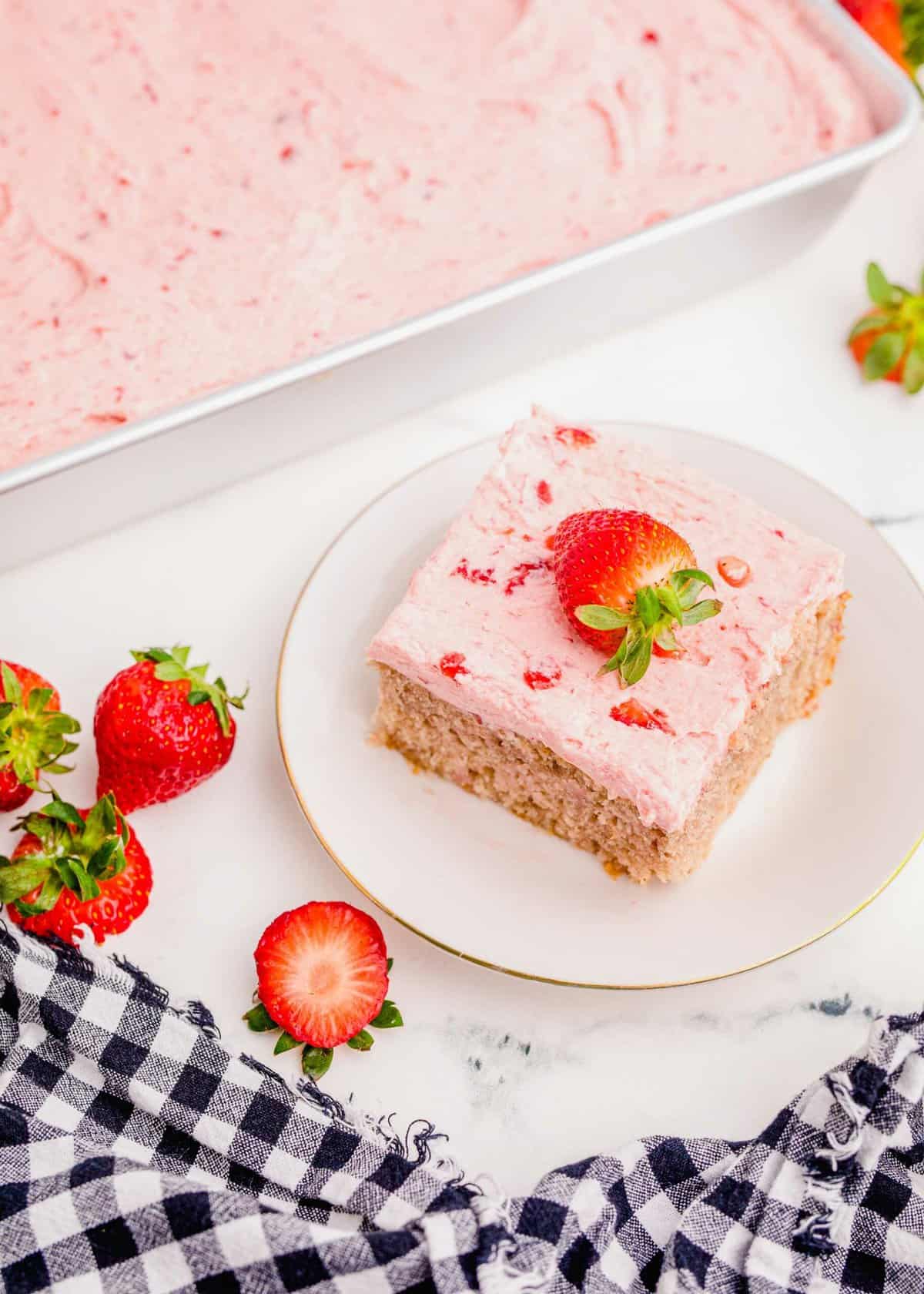 Piece of strawberry sheet cake on plate, with pan of cake in background