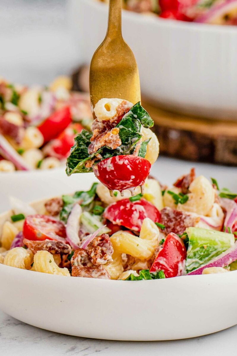 A fork is removing a bite sized portion of pasta salad from the bowl. 