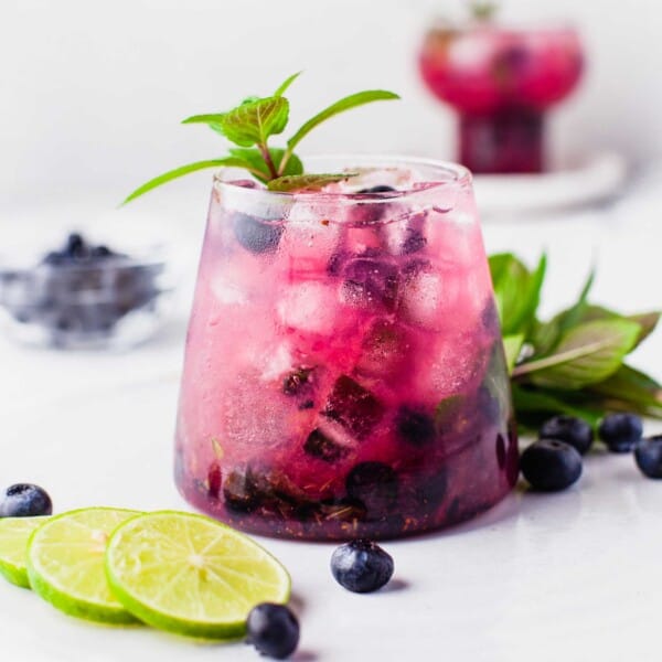Blueberry mojito on round tray with lime slices, berries, and mint