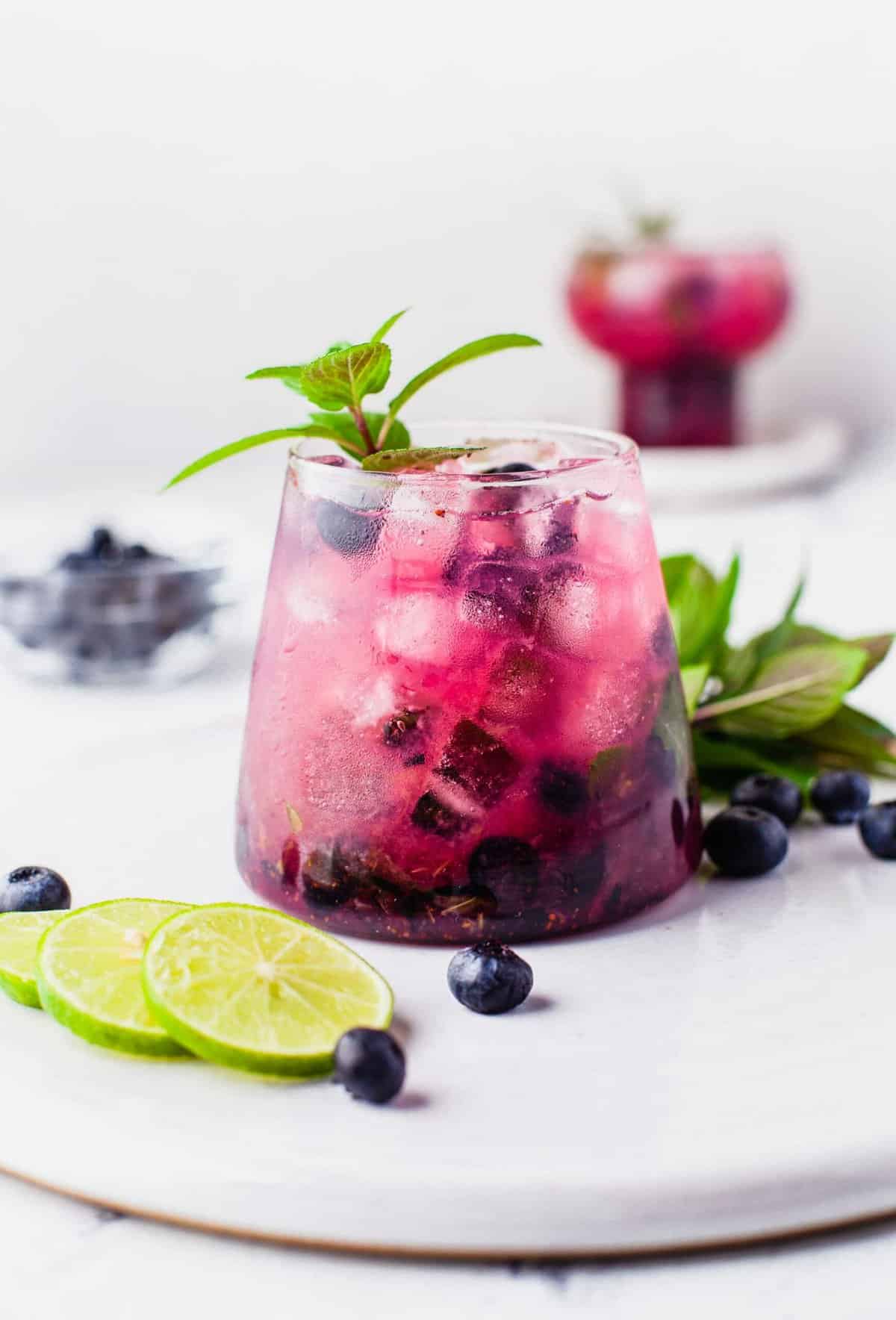 Blueberry mojito on round tray with lime slices, berries, and mint