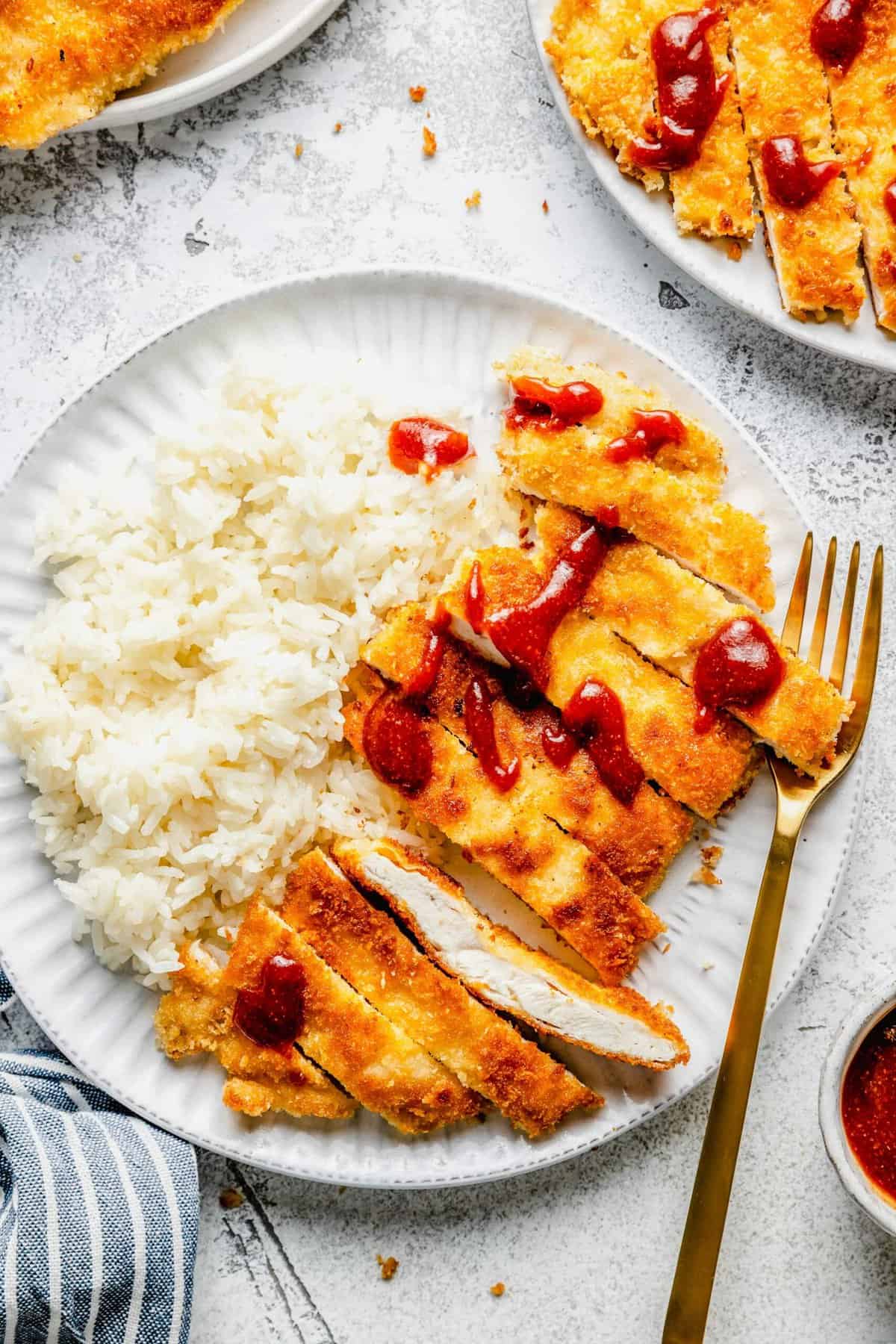 Overhead view of a plate with white rice, a fork, and sliced chicken katsu topped with tonkatsu sauce