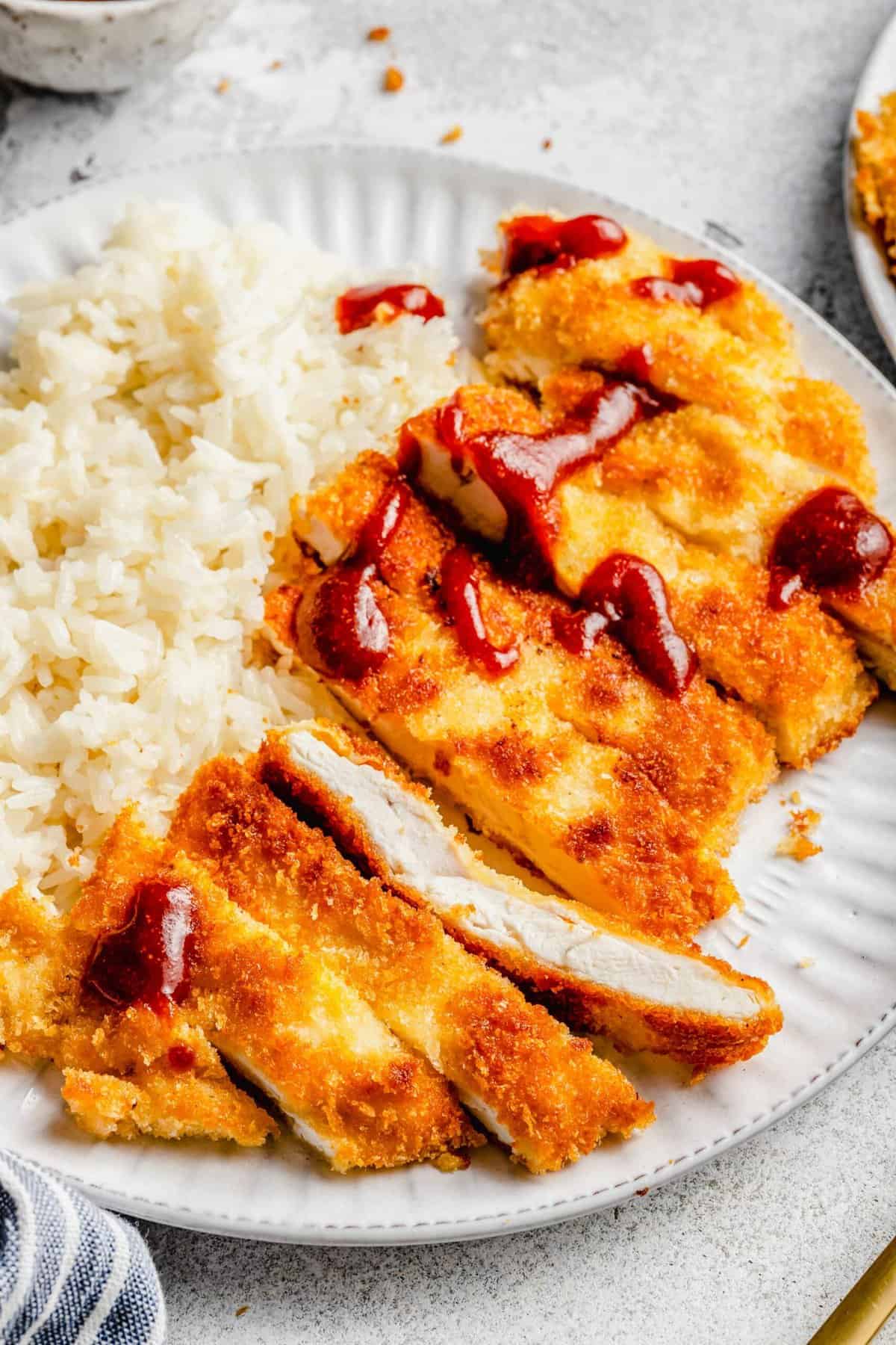 A plate with white rice and slices of chicken katsu topped in tonkatsu sauce