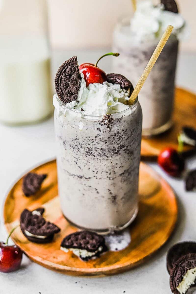 A milkshake is placed on a small wooden plate with Oreo cookie pieces surrounding it. 