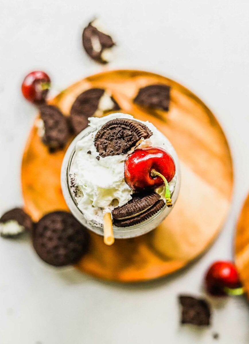 The top of a milkshake is topped with a straw, a cherry, a halved Oreo cookie, and whipped cream. 