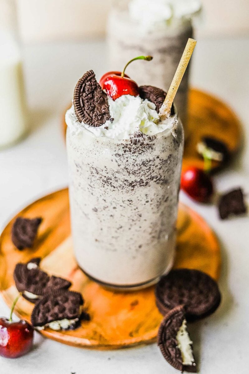 A full glass of Oreo milkshake is topped with a cherry, cookies, and whipped cream. 