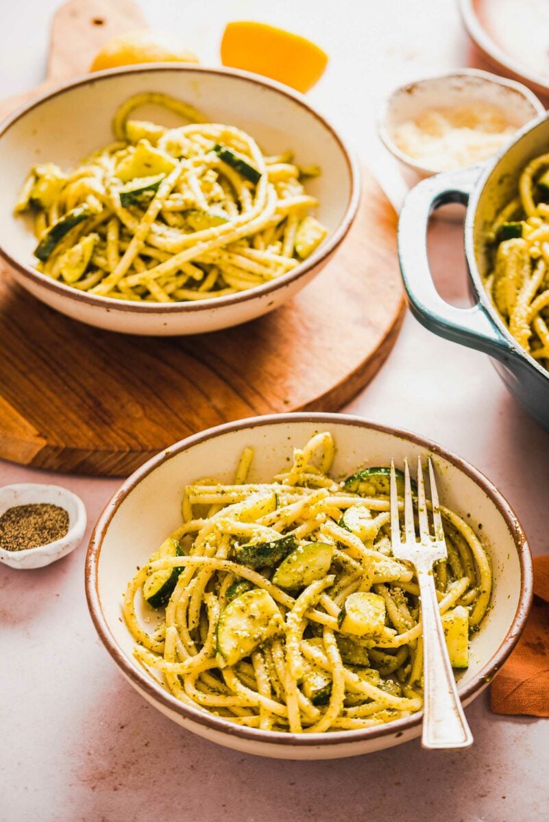 A fork is placed in a white bowl filled with pasta and zucchini. 