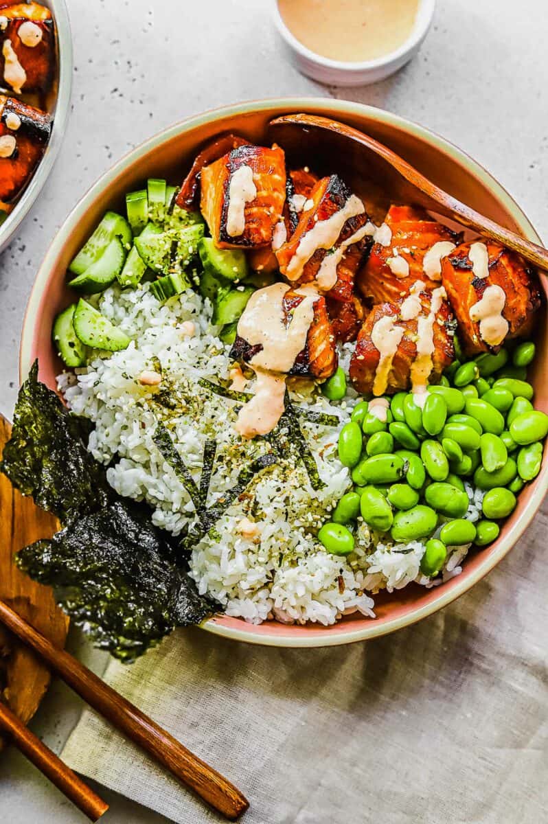 Rice, seaweed, edamame, and cucumbers are placed next to rice and salmon in a bowl. 