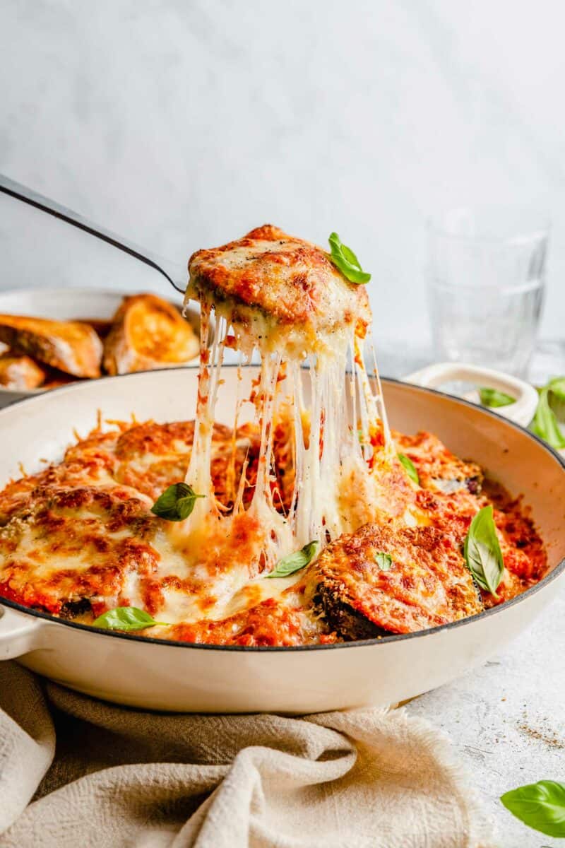 slice of eggplant parmesan being lifted out of pan and cheese pull can be seen