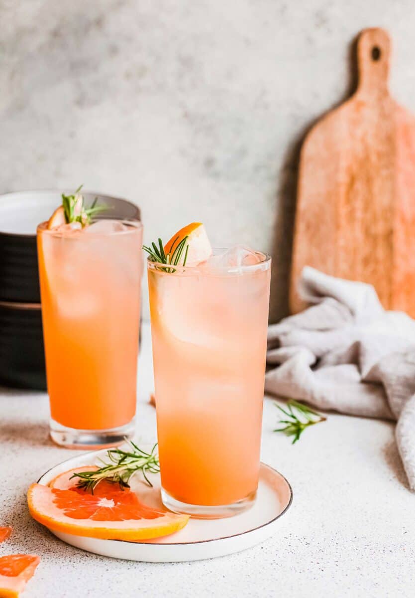 Two glasses of gin and tonic are placed on a white countertop. 