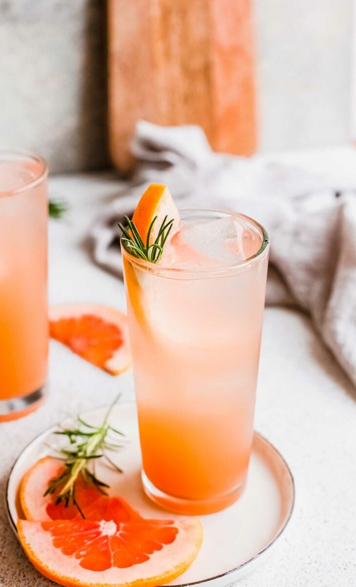 A glass of grapefruit gin and tonic is garnished with rosemary and grapefruit. 