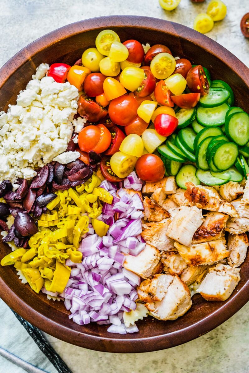 The ingredients for greek chicken pasta salad are all placed alongside each other in a mixing bowl. 
