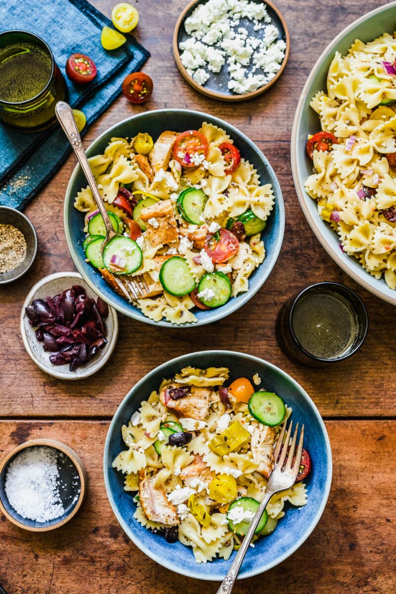 Two bowls are filled with servings of greek pasta salad. 
