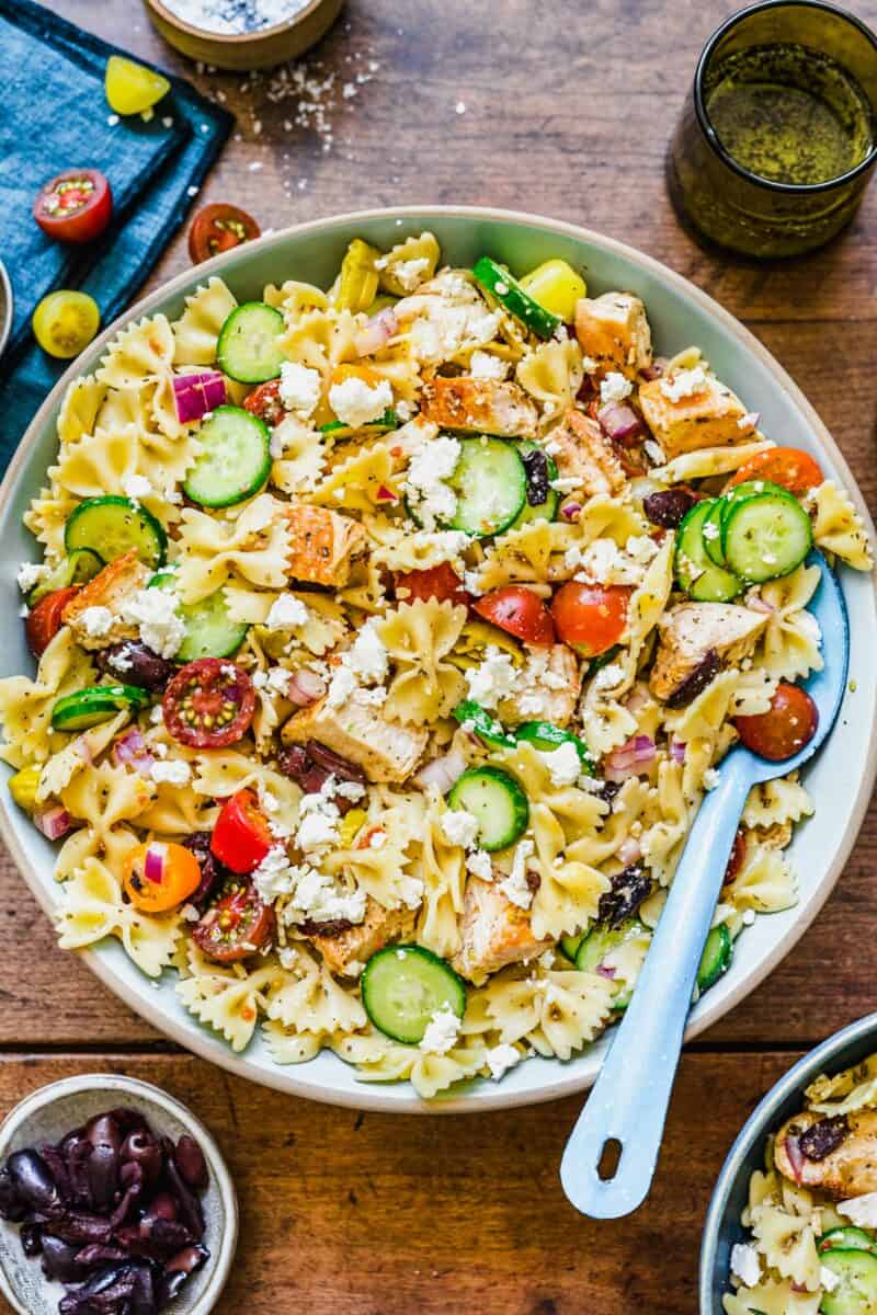 A large greek chicken pasta salad is served in a large bowl with a serving spoon.